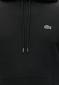 Sweat à capuche noir avec des cordons assortis et un petit logo crocodile vert brodé sur la partie supérieure gauche de la poitrine.