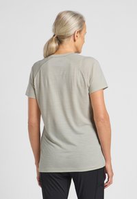 T-shirt sportivo grigio chiaro a maniche corte, con texture liscia, cuciture raglan e scollatura arrotondata, indossato con pantaloni neri.