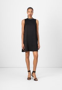 Black sleeveless dress with a round neckline; smooth fabric, relaxed fit, and a-line shape. Worn with black high-heeled sandals.