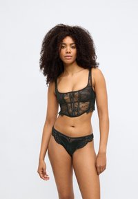Zestaw czarnej koronki bielizny składający się z dopasowanego przezroczystego biustonosza z konstrukcyjnym fasonem i kwiatowym wzorem, w zestawie z pasującymi koronkowymi stringami.
