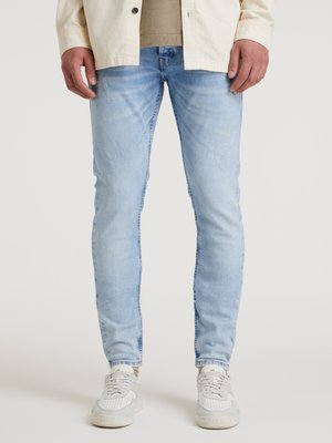 Jeans in denim blu chiaro con una vestibilità slim, caratterizzati da aree sbiadite e leggere sgualciture, abbinati a sneakers bianche.