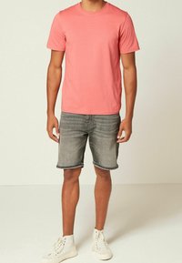 Koronowy t-shirt z krótkim rękawem połączony z szarymi szortami dżinsowymi i białymi trampkami na wysokiej podeszwie. Materiał jest gładki; szorty mają podwinięty brzeg.