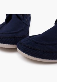 Navy canvas slip-on shoes with a stitched seam, textured rubber sole, and rounded toe design. Minimalistic with gold-tone eyelets.