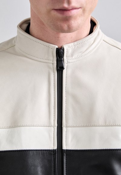 Leather jacket featuring a cream upper section and black lower section, with a stand collar and front zipper. Smooth texture and stitching detail.