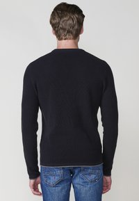 Granatowy sweter ribbed z długimi rękawami i okrągłym dekoltem, wykonany z teksturowanej tkaniny, w połączeniu z jasnoniebieskimi dżinsami.