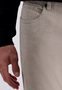 Beige Hose mit einem dezenten Karo-Muster aus einem glatten Stoff. Verfügt über eine Vordertasche und eine leichte Textur.