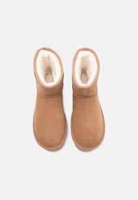Botines de ante marrón con un suave forro de piel sintética blanca, puntera redondeada y caña corta, que presentan un simple detalle de costura.