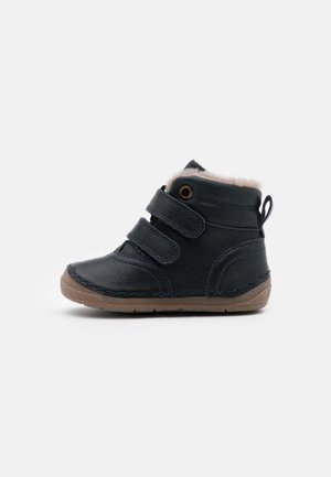 Botte noire pour tout-petit avec deux sangles Velcro, semelle en caoutchouc beige, doublure en fourrure douce et languette de traction sur fond blanc.