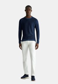 Maglione a maglia testurizzata blu navy, jeans bianchi e sneakers blu navy. Il maglione presenta un collo a girocollo e polsini a coste; l'outfit ha una vestibilità casual.