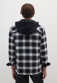 Schwarz-weißer Karoshemd mit schwarzer Kapuze, Knopfverschluss vorne, langen Ärmeln und hochrollbaren Bündchen. Glatte Textur.