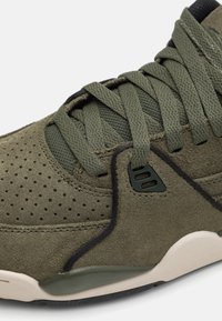 Olivgrön mockaskor med texturerad yta, perforerade detaljer, platta snören och svarta accenter; har en beige sula.