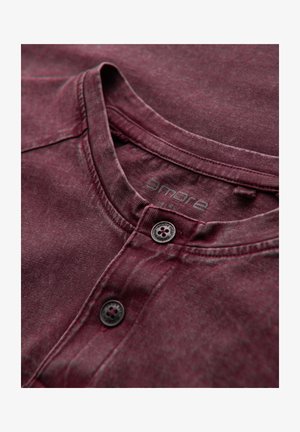 Maglietta henley in cotone borgogna con finitura testurizzata, dotata di scollatura tonda, due bottoni neri e un logo del marchio stampato in modo discreto.