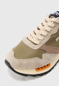 Μπεζ και ελιάς πράσινο σουέντ αθλητικό παπούτσι με κρέμ κορδόνια, μαύρη σόλα, πορτοκαλί λεπτομέρεια στη μέση της σόλας και λογότυπο στη γλώσσα και στα πλευρικά πάνελ.