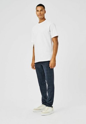 Una camiseta blanca de algodón combinada con pantalones de cuadros azul marino y zapatillas blancas. El conjunto presenta un corte relajado y elementos de diseño sencillos.