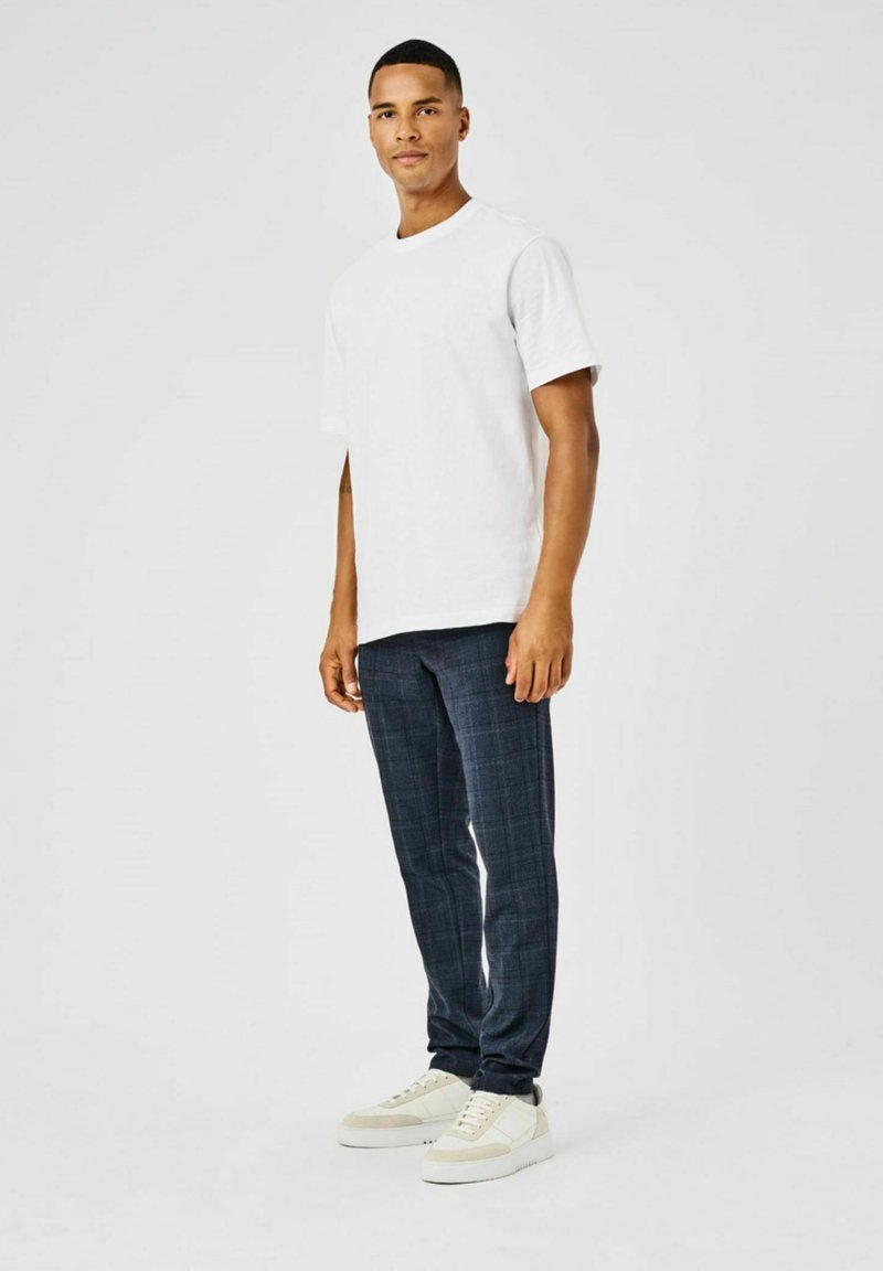 Una camiseta blanca de algodón combinada con pantalones de cuadros azul marino y zapatillas blancas. El conjunto presenta un corte relajado y elementos de diseño sencillos.