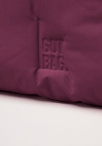 Fioletowa torba z tkaniny o gładkiej fakturze, z wytłoczonym logo "GOT BAG" po bokach. Prosty design, solidna konstrukcja.