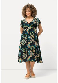 Ein schwarzes Kleid mit einem farbenfrohen geometrischen und floralen Muster, ausgestattet mit kurzen, flatternden Ärmeln und einem V-Ausschnitt, kombiniert mit Plateausandalen.