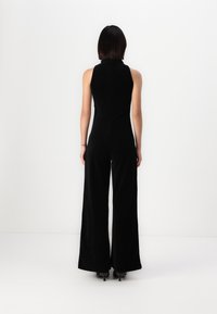 Mono de terciopelo negro con un cuerpo ajustado y pantalones de pierna ancha. Presenta un escote alto y una textura suave. Diseño minimalista.