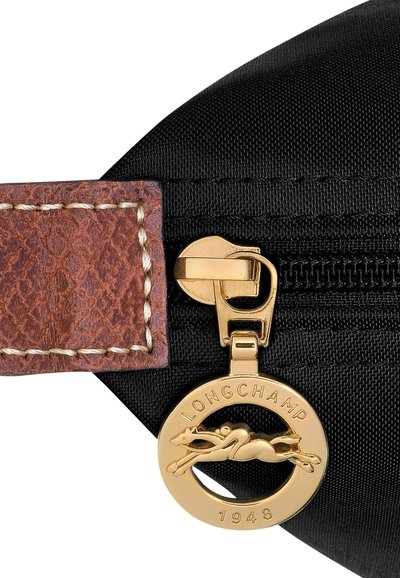Black nylon bag with a brown leather accent, featuring a gold zip pull and a circular charm depicting a leaping horse, engraved "LONGCHAMP 1948."
