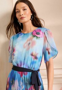 Virágmintás ruha átlátszó anyagból, kék árnyalatú, rózsaszín és lila virágokkal, puffos ujjakkal és fekete derékövével.