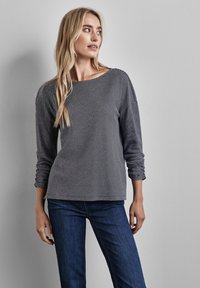 Grau gestreiftes Langarmoberteil mit Rundhalsausschnitt und raffinierten Ärmeldetails, kombiniert mit dunkelblauen Jeans; glatte Baumwollstofftextur.