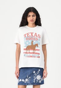 Hvit bomull t-skjorte med grafisk trykk som har "TEXAS RODEO" i rødt, blå stjerner, og en silhuett av en hest og rytter.
