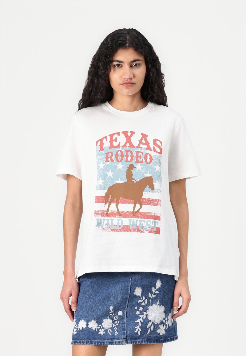 Hvit bomull t-skjorte med grafisk trykk som har "TEXAS RODEO" i rødt, blå stjerner, og en silhuett av en hest og rytter.