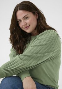 Lysegrøn strikket sweater med ribstrikkede, puffede ærmer. Rund halsudskæring og tætsiddende manchetter. Båret over denim, med en blød tekstur.