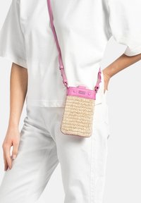 Sac en bandoulière en paille tissée avec des accents en cuir rose, de forme rectangulaire, avec une sangle ajustable et une fermeture à pression sur le dessus.