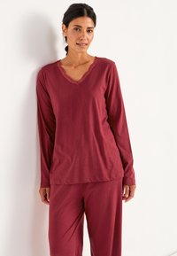 Burgundy loungewear-set som innehåller en långärmad topp med spetskantad V-ringning och matchande byxor, tillverkade av mjuk, slät tyg.
