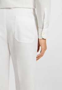 White linen trousers with a back pocket featuring a rectangular shape. The fabric has a light, textured appearance.