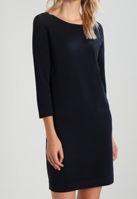 Marinblå, långärmad klänning med båthals. Tillverkad av slät tyg, har en rak silhuett och knä-lång design. Enkelt och klassiskt stil.