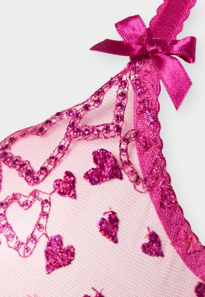 Διαφανές ροζ ύφασμα με λαμπερά σχέδια σε σχήμα καρδιάς, περιγραμματισμένα με ροζ στρας, και ολοκληρωμένο με ροζ σατέν φιόγκο στο λουράκι.