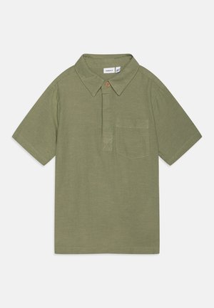Polo de manga corta en verde oliva, confeccionado en una tela texturizada, con cuello, un bolsillo en el pecho y un detalle de botón marrón.