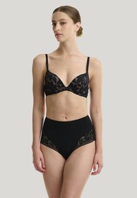 Soutien-gorge en dentelle noire avec un décolleté plongeant et de fines bretelles ajustables, associé à une culotte noire taille haute avec des accents en dentelle sur les côtés.