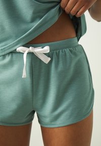 Ljus teal-shorts i mjukt tyg, med en elastisk midja och en vit dragsko. Slät yta, enkel design och utan mönster.