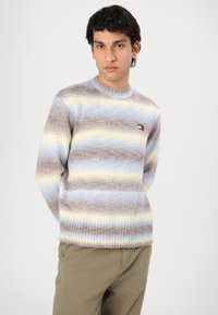 Knitted sweater in soft yarn featuring horizontal stripes in brown, light blue, and yellow. Ribbed neckline and hem; logo patch on chest.