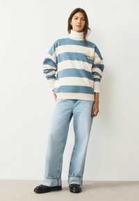 Blue and white striped sweatshirt with a high collar, featuring text detail, paired with light blue wide-leg jeans and black chunky shoes.