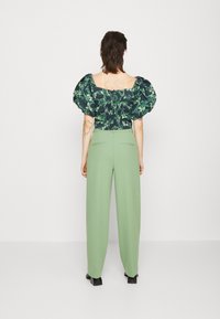Top verde scuro con motivo floreale e maniche a sbuffo, abbinato a pantaloni alta vita verde chiaro. L'outfit presenta una zip sul retro e una forma strutturata.