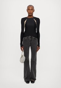 Top nero a maniche lunghe con lati a motivo crema, abbinato a jeans grigi scuri a zampa d'elefante e una piccola borsa testurizzata. Scarpe nere completano l'outfit.
