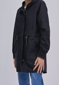 Černá větrovka s kapucí, zipovým zapínáním, dvěma předními kapsami a šňůrkami v pase. Hladká textura, volný střih.