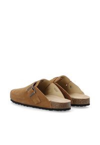 Zapatos tipo slip-on de ante marrón con una punta amplia, plantilla de corcho y detalle de hebilla de metal plateado en el costado, que cuentan con una suela de goma negra Texturizada.