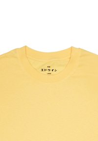 T-shirt in cotone giallo con scollatura a girocollo. L'etichetta mostra "LARGE" in testo nero insieme a caratteri giapponesi. Texture liscia e colore uniforme.