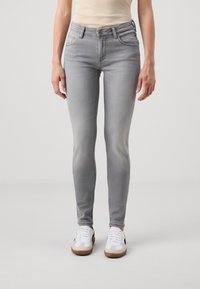 Grå smala jeans med en blekt finish, fem fickor och hög midja; kombinerat med vita sneakers med bruna detaljer.