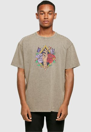 Beige oversized T-shirt med en ribbet halskant. Har et farverigt grafisk design af blomster, sommerfugle og en hånd i midten.