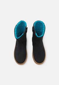 Czarne zamszowe botki z turkusową sztuczną futrzaną wyściółką, krótkiego fasonu, z bocznymi zamkami błyskawicznymi i jasnobrązową gumową podeszwą, widziane z góry.