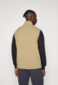 Giacca a blocchi di colore nei toni beige e nero, con colletto alto e un tessuto leggero e morbido. Polsini aderenti con una vestibilità comoda.