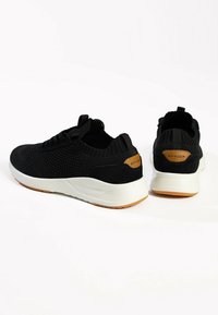 Black athletic shoes with breathable knit upper, white sole, brown accent on heel, and textured pattern for enhanced grip.