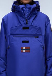 Blue waterproof jacket with a high collar, front pocket, black zippers, and a Norwegian flag patch on the chest. Smooth texture.