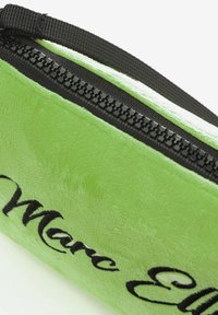 Astuccio verde in peluche con una cerniera nera e testo ricamato. Texture morbida e forma arrotondata. L'esterno mostra un colore vivido.